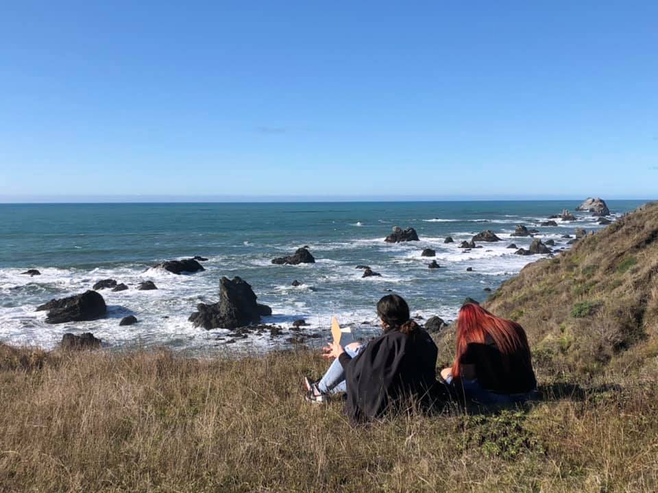 two Elsie Allen high school students sit on a bluff above the ocean journaling and sitting in the sun.