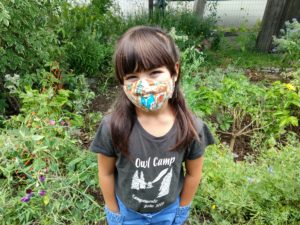 little girl smiling in a face mask and owl camp t-shirt,