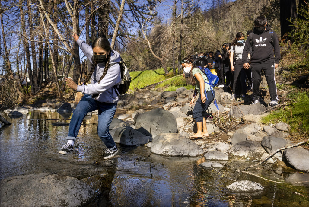 Students from Roseland Accelerated Middle School hope across the creek at Rancho Mark West on their way to help mulch some of the 4,000 replanted trees on the property on Thursday, February 10, 2022. (Photo by John Burgess/The Press Democrat)